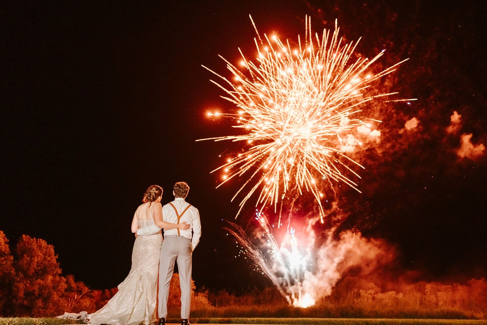 Newlyweds watching a golden Schneitter fireworks finale light up the night sky